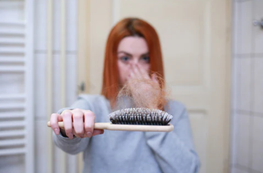 A redhead or red haired woman shocked at the amount of hair on her hair brush. Concept of hair loss, cultural traditions with hair, hair styles, thinning hair.